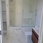 white tile shower backsplash with elaborate configuration, sliding glass shower doors, seamless white tiling and floating wooden vanity