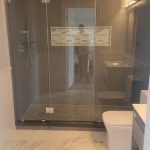 Glass shower enclosure and new shiny white tiles in modern bathroom