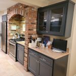 Unique kitchen with brick enclosure around range with dark modern cabinetry and bright countertops